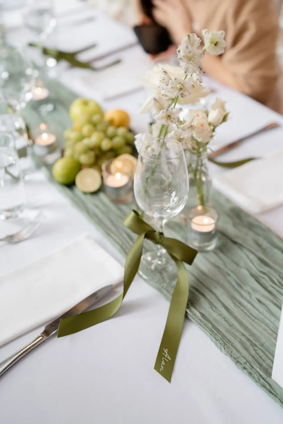 Olive ribbon place name tied to a wine glass beside white delphiniums