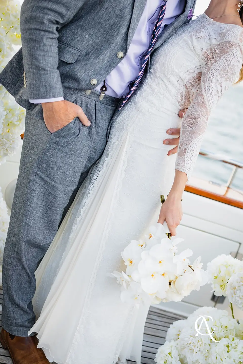 Close view of a white phalaenopsis orchid bouquet held against a long-sleeved lace wedding gown