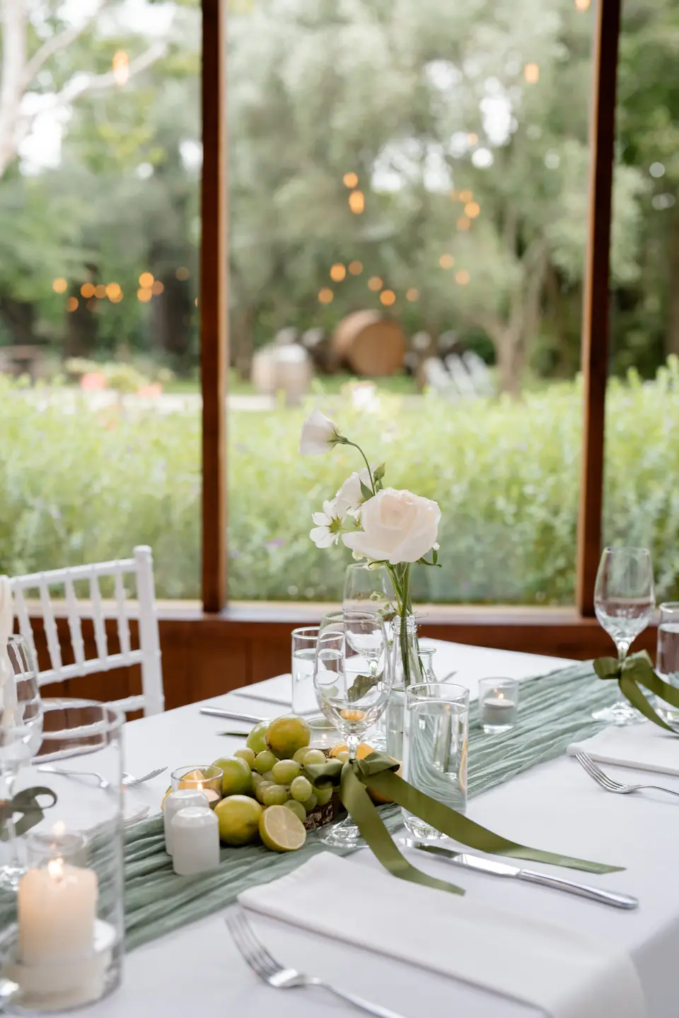 Single white rose bud vase beside limes and grapes on a reception table