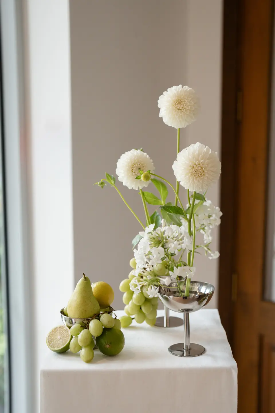 White dahlias and phlox in silver coupes with pears, limes and grapes