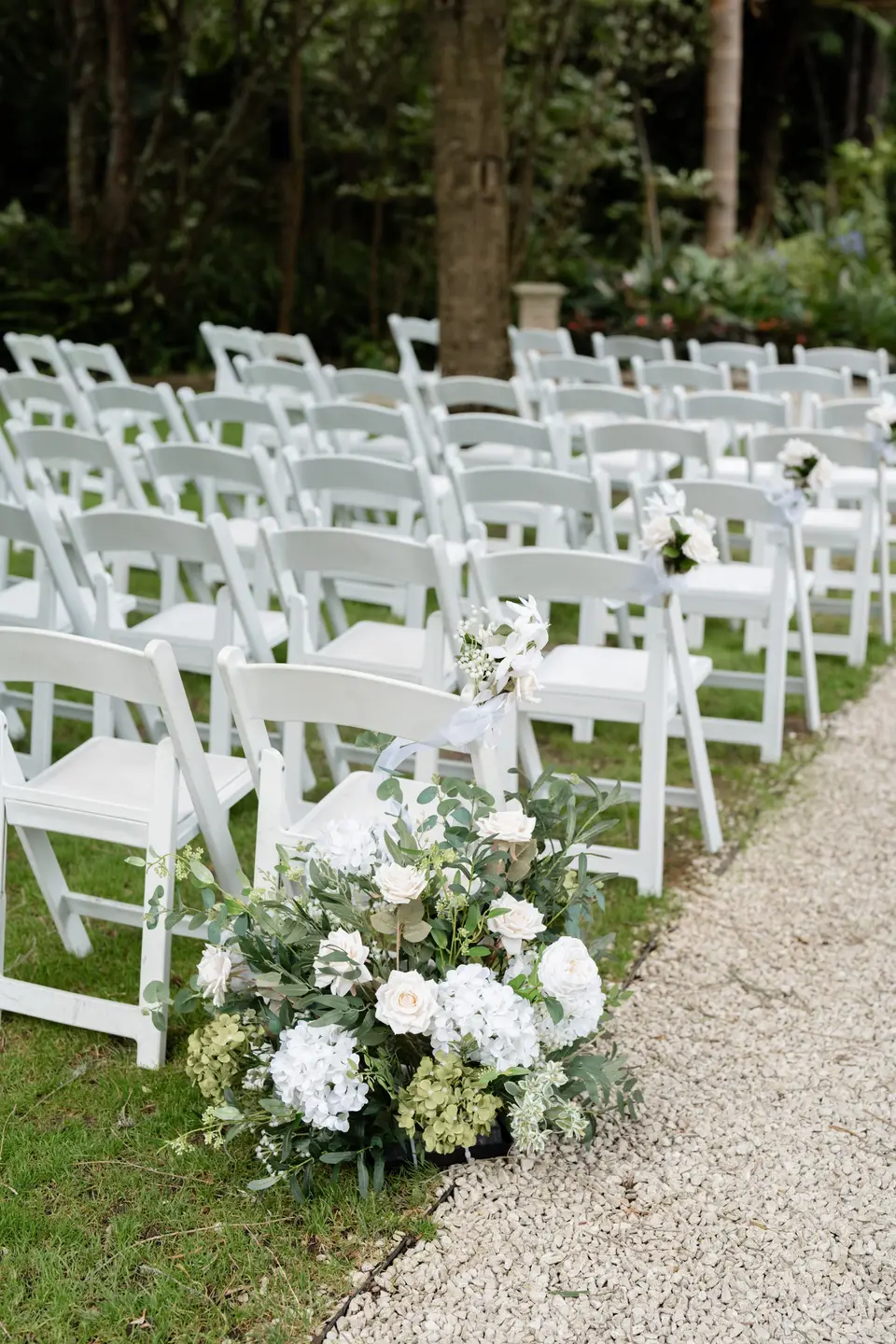 White hydrangea and rose aisle arrangement beside white ceremony chairs at Markovina