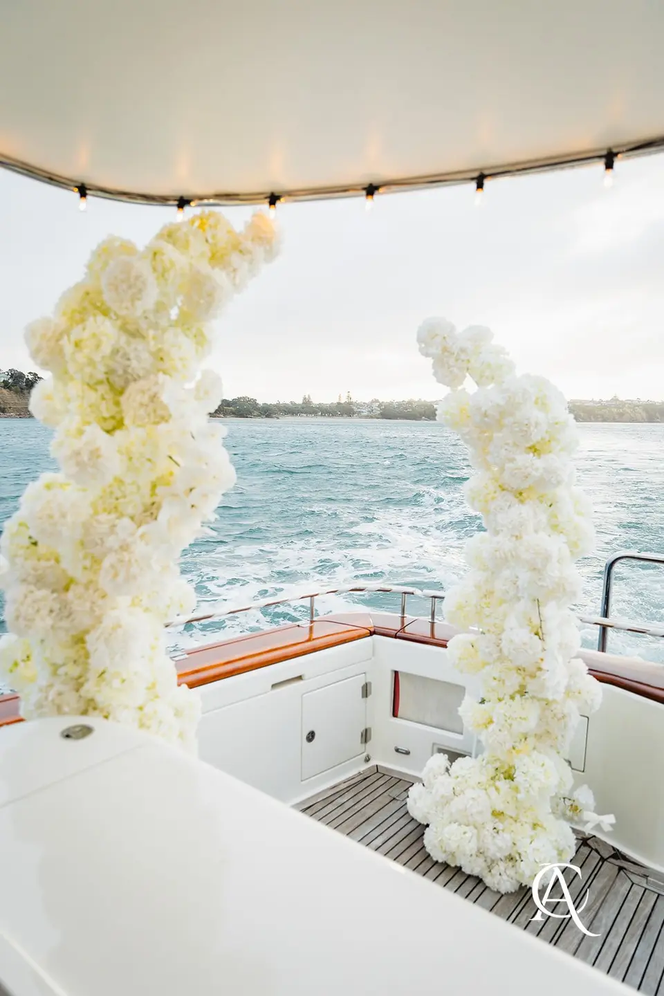 White hydrangea columns standing on a yacht's aft deck as the boat moves, with its wake trailing behind