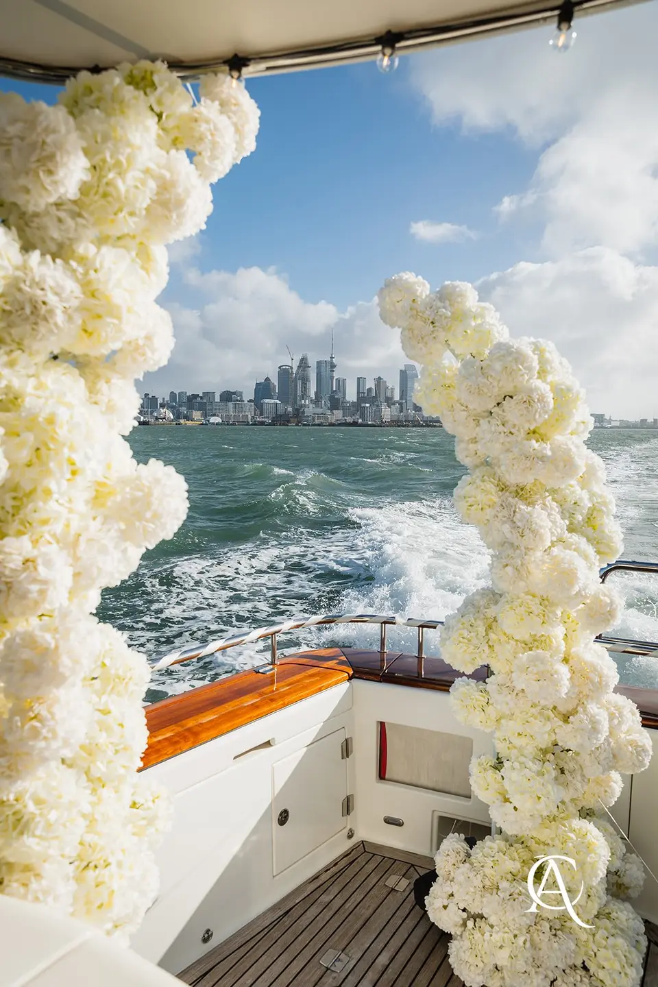 Two columns of white hydrangea framing the aft deck of a yacht, with the Auckland city skyline and Sky Tower across the harbour
